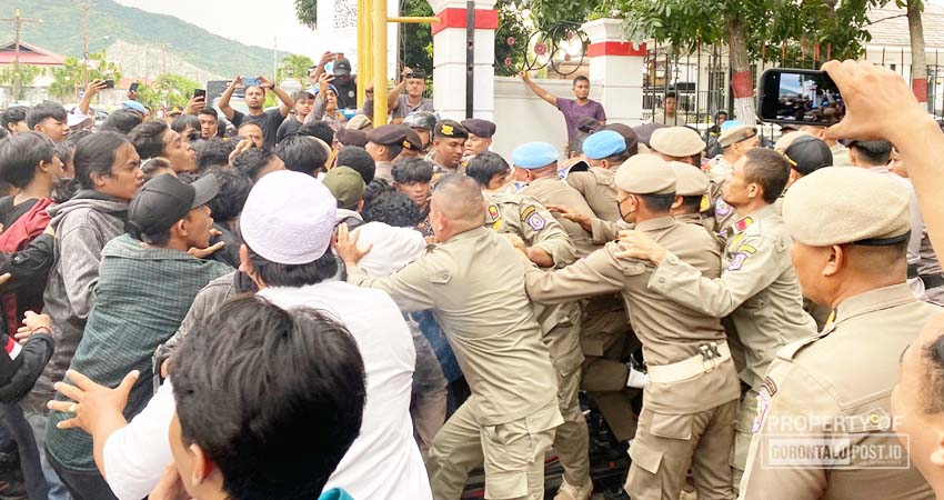 Aksi dorong antara massa aksi dengan petugas Satpol PP serta petugas kepolisian di depan Rudisgub yang membuat demo menjadi ricuh buntut massa aksi merobohkan pintu pagar Rudisgub, Senin, (01/07/2024). (Foto: Suciamanah/Gorontalo Post).