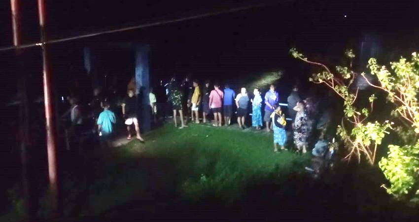 Warga yang menggunakan penerangan seadanya berdiri di pintu air Bendungan, mencari korban hanyut, Rabu (05/03/2025).