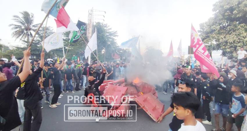 Massa tampak menarik pembatas jalan plastik merah ke arah kobaran api, memperbesar kobaran api, Senin (1/9/2025). (F. Natha/Gorontalo Post)
