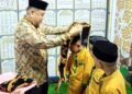 WISUDA. Kabag Kesra saat mengalungkang selempang pada para wisudawan.