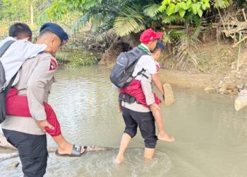Petugas kepolisian Brimob Polda Gorontalo membantu warga, khususnya anak-anak sekolah, menyeberangi sungai akibat putusnya jembatan gantung yang menjadi akses utama masyarakat, Selasa (14/01/2026).