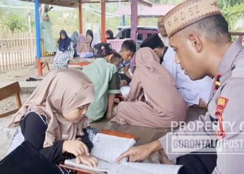 Kapolsubsektor Dengilo, Ipda Adam Ahmad,S.H.,CBLS.,CCrp.,CPS. saat mengajari baca tulis Al-Qur’an kepada anak-anak yang ada di Kecamatan Dengilo. (F. Zulkifli Tampolo/ Gorontalo Post)